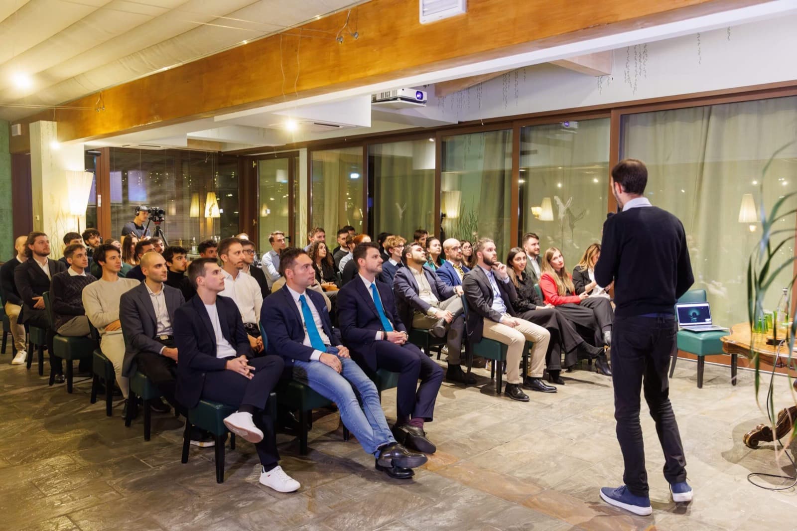 Un collega presenta davanti a una platea di una trentina di persone sedute, durante un evento serale in azienda